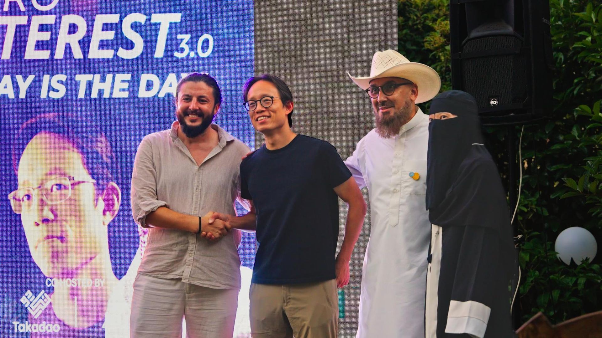 Group of people posing in front of a digital display at an outdoor event.