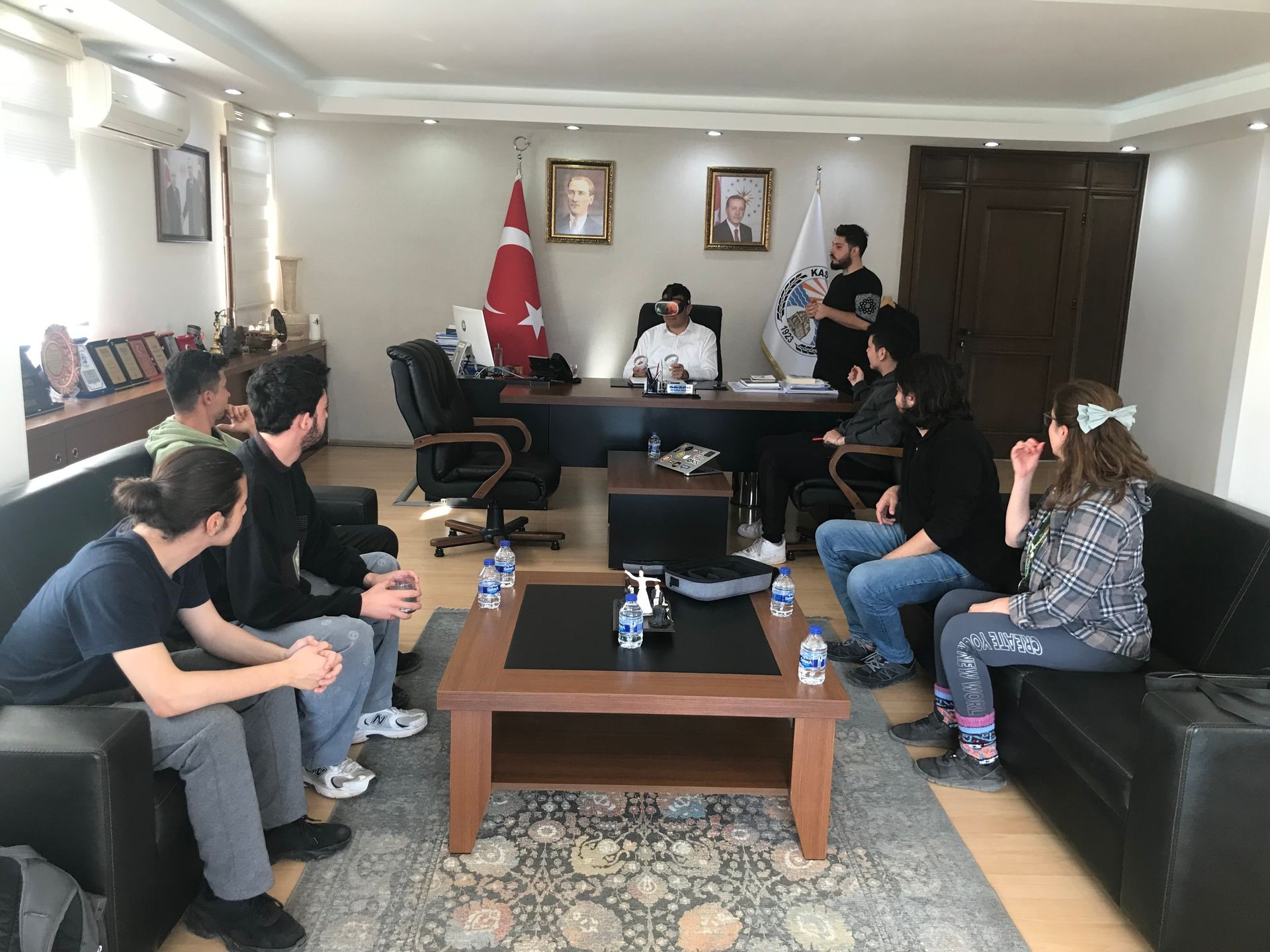 Group of people having a discussion in an office with Turkish flag and portraits on the wall.