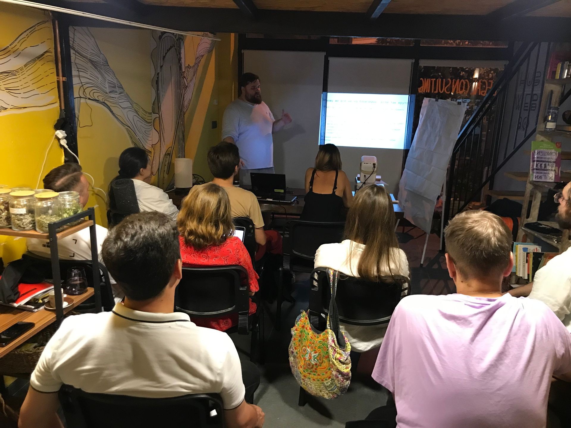 A group of people sitting in a room watching a presentation projected on the wall.