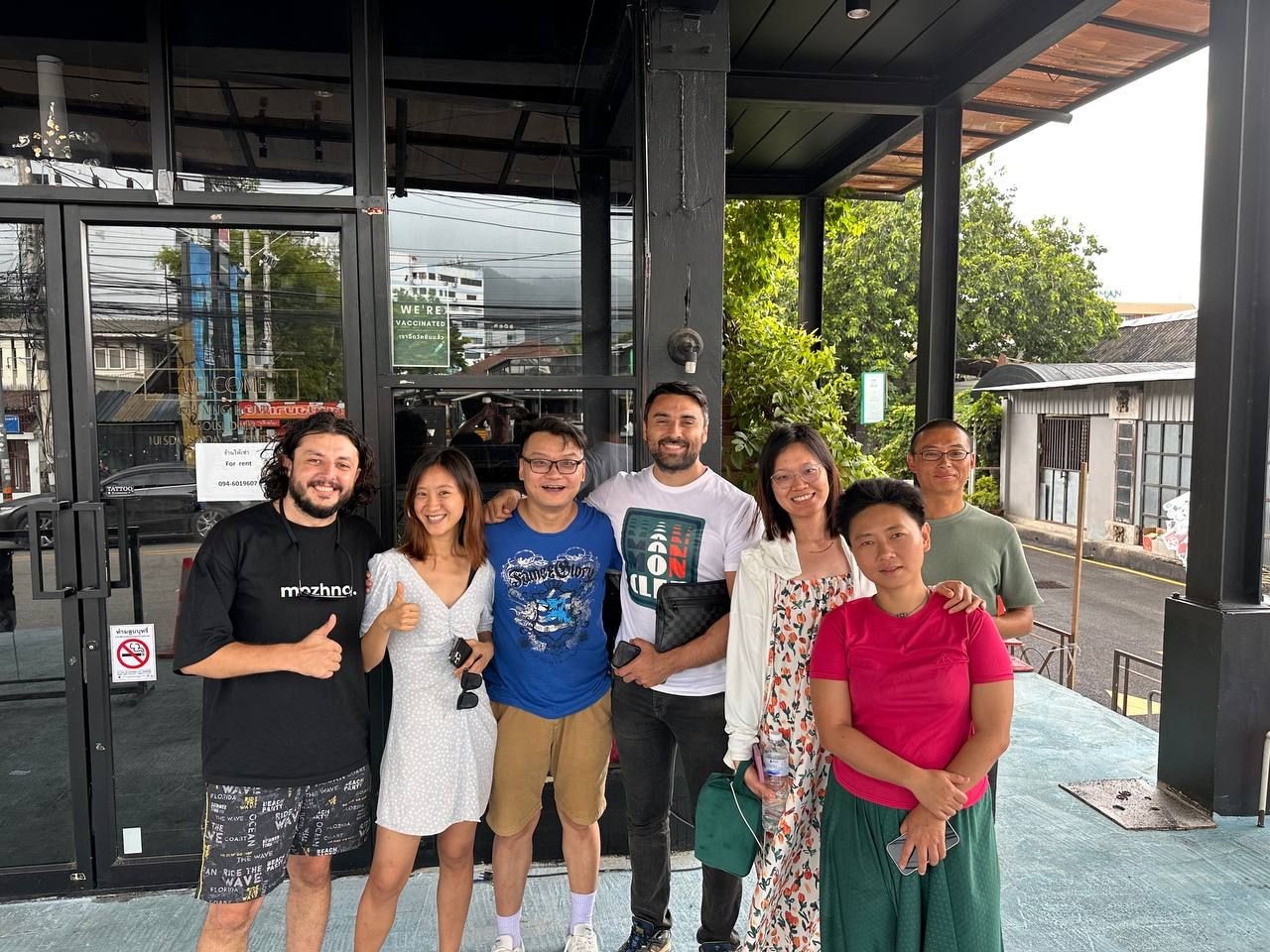 Group of seven people smiling and posing for a photo outside a building.