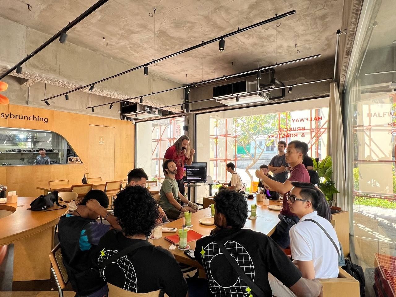 Group of people gathered around a table in a modern cafe with large windows.