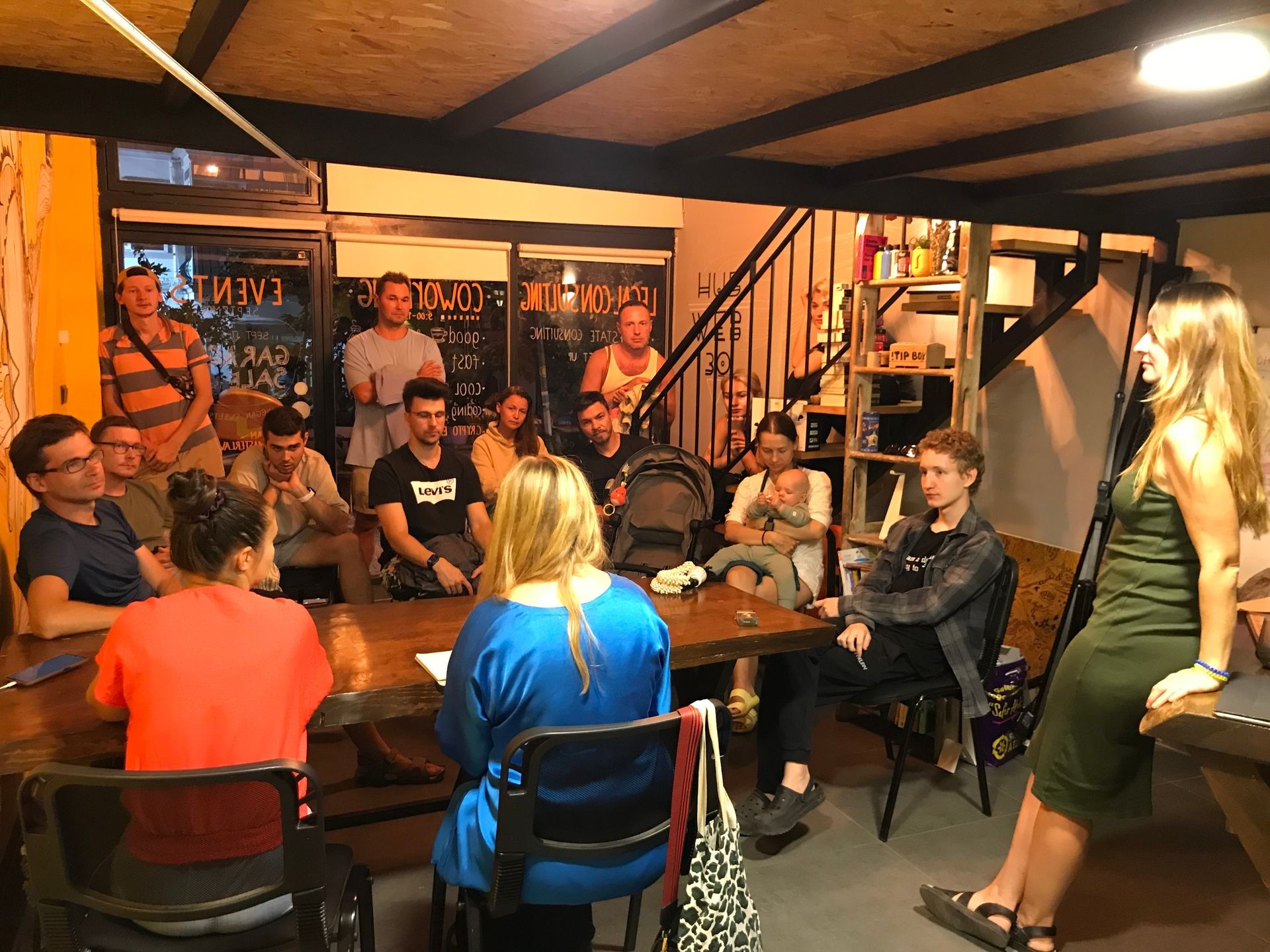 Group of people gathered in a cozy room for a meeting, with one person standing and speaking.