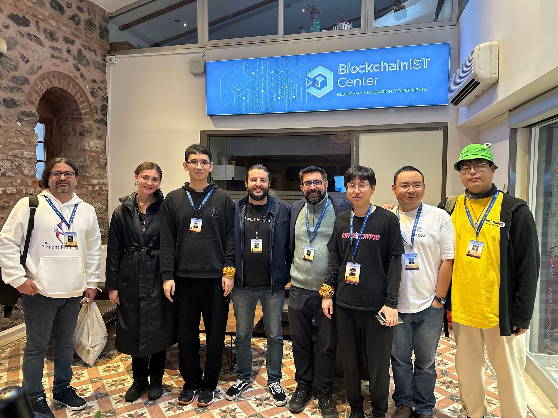 Group of people standing indoors at BlockchainIST Center, wearing conference lanyards.